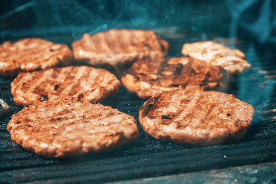 Hamburger patties and other meat cooking on a hot grill with smoke, preparing food for a summer barbecue