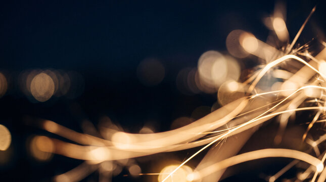 Bright burning sparkler trails against a dark night sky with warm golden bokeh lights