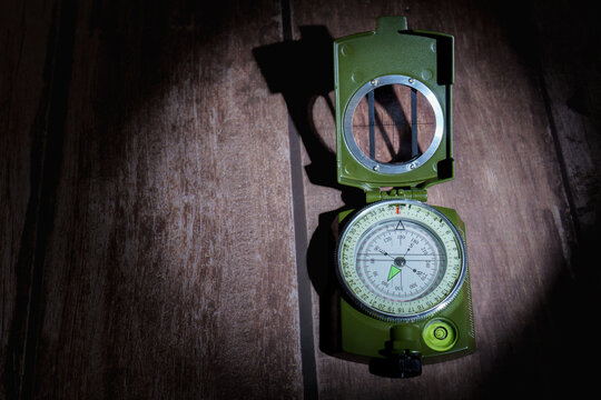 Green military compass tool for navigation and exploration, showing north direction on a dark wooden background