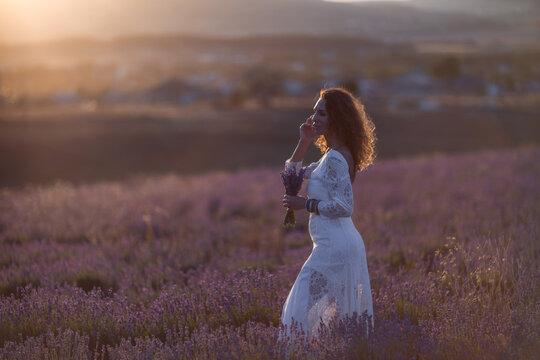 Woman lavender field at sunset holding flowers in white lace dress
