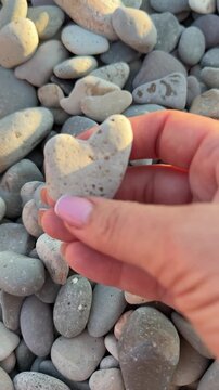 Heart-shaped pebble found on a rocky beach by woman during golden hour. Close-up high angle shot.