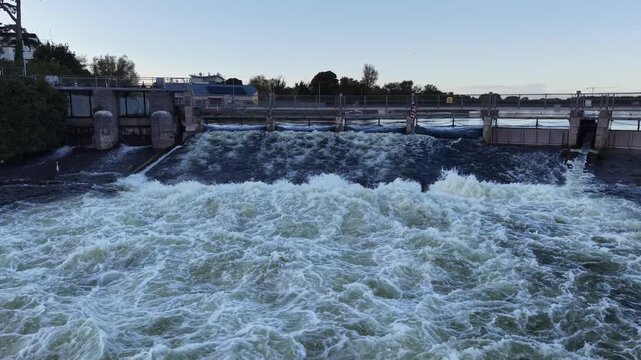 Powerful water flows through Salmon Weir on the River Corrib in Galway City Ireland, creating turbulent whitewater below the weir gates.