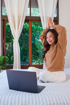 Vertical portrait of a woman meditating or practicing yoga on bed in front of laptop computer