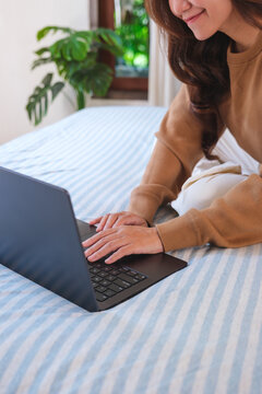 Vertical closeup of a woman using and working on laptop computer while sitting on bed at home