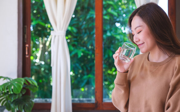 Portrait image of a woman holding and drinking water at home