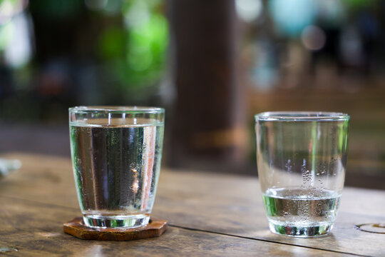 Clear water glass and low water glass on rustic wooden table, creating quiet comparison of fullness and transparency in soft natural light