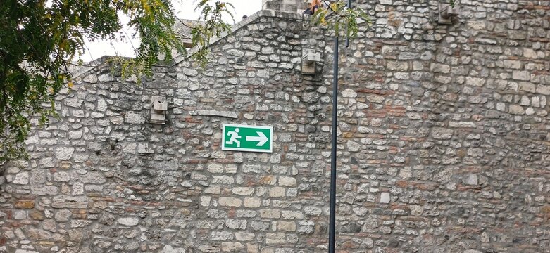 Gr&uuml;nes Notausgang-Fluchtwegschild mit Pfeil nach rechts auf einer rustikalen historischen Steinmauer
