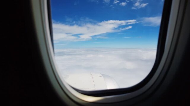 Airplane wing above sunlit clouds seen through window