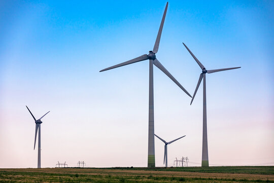 Large modern wind turbines on a green field against a clear blue sky, symbolizing renewable energy and sustainability.