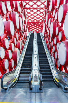 An outdoor escalator. On both sides are red drums.