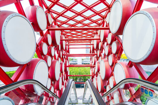 An outdoor escalator. On both sides are red drums.