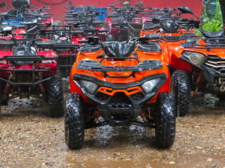 Orange all terrain vehicle parked among red quad bike fleet on wet gravel, rugged tires and protective frame creating adventurous outdoor recreation scene for rental service © CoreRock