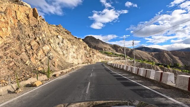 A vehicle climbs a paved road through barren rocky terrain with concrete barriers and distant snow-capped peaks with scatte - Spiti Valley Himachal Pradesh India | Himalayan road trip GoPro dashcam 4K
