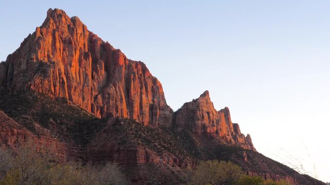 Scenic view from a moving car of the majestic red rock mountains in zion national park, utah, beautifully illuminated by the warm light of the setting sun against a clear blue sky