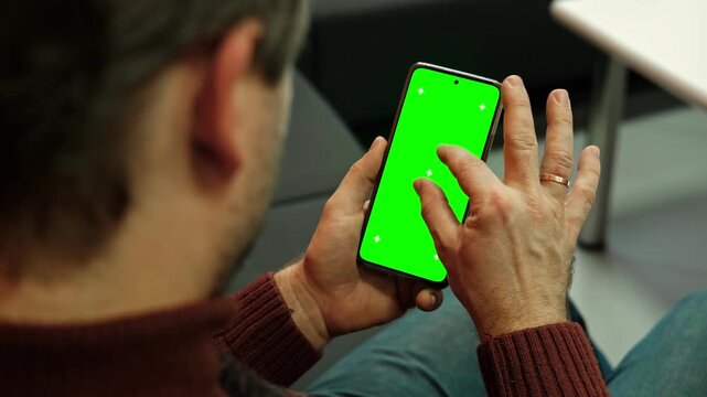 Male user tapping gestures on digital cellular display smartphone template mockup with green screen chroma key tracking markers. Over shoulder perspective closeup view inside office. Landscape footage