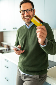 Entrepreneur receiving payment with multiple credit cards and smartphone, smiling while managing business finances and online transactions from a home environment