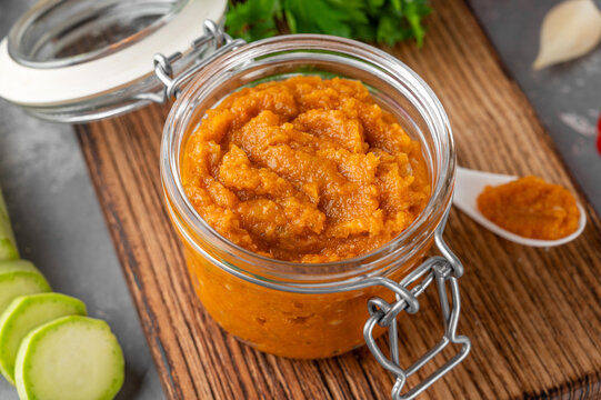 Zucchini caviar in a glass jar with fresh vegetables and herbs on a rustic board, homemade vegetable spread for healthy eating and canning.