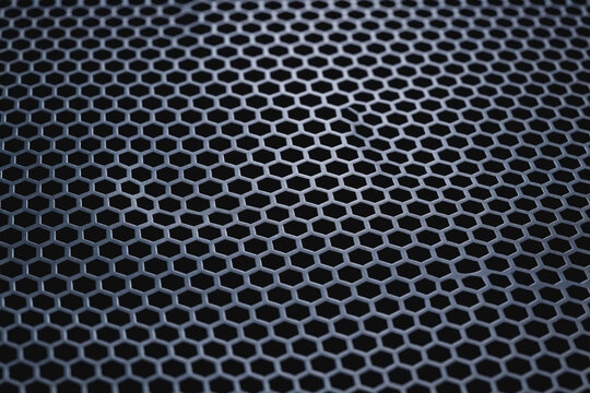 A close-up macro shot of a uniform hexagonal metal perforated mesh surface, showing its detailed geometric pattern and texture.
