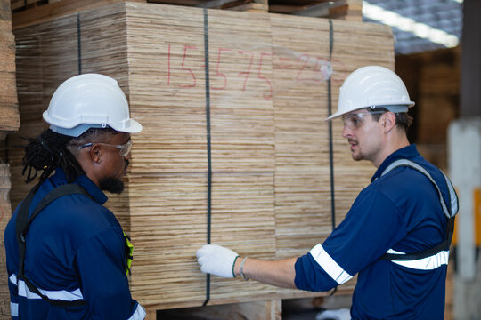 Team meeting: factory workers show teamwork as two men talk beside stacked plywood and a man touches the strapping.