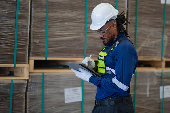 During export packaging inspection, a man records an export shipment on a tablet beside wrapped pallets in the warehouse.