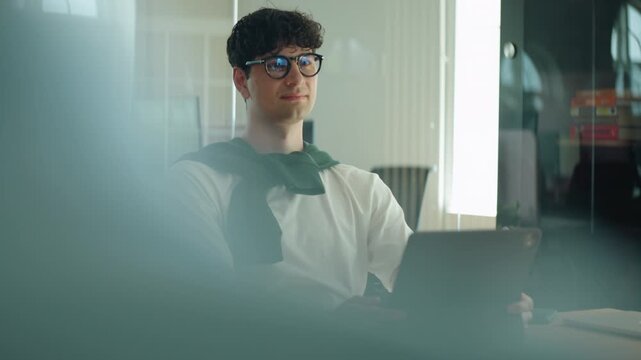 Man sits at a desk listening and smiling during a business meeting in a modern office, representing work, communication, engagement, and presence in a workplace discussion.