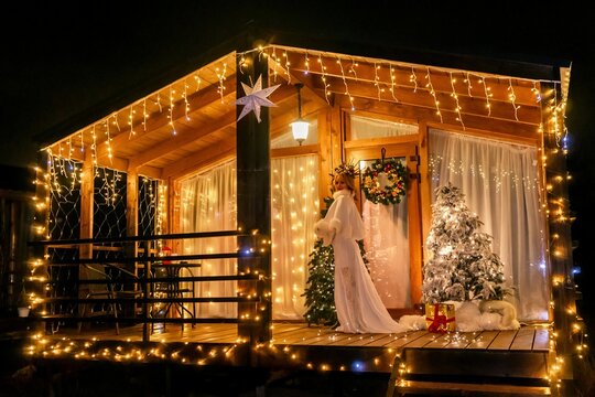 Christmas Lights Cabin Decor Night A wooden cabin decorated for Christmas with lights and a Christmas tree.