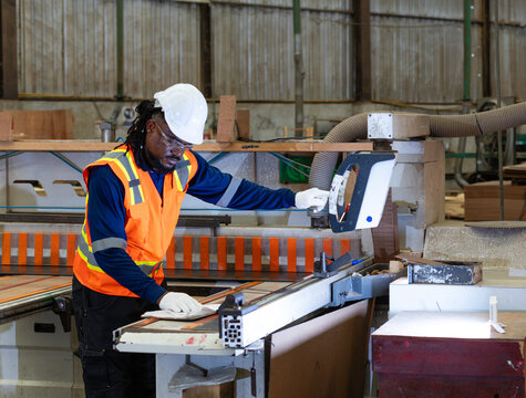 Inside a woodworking shop, a carpenter manages plywood work while operating the control panel beside a panel saw.