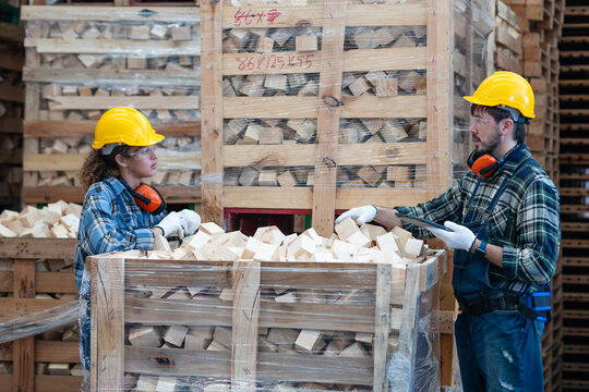 Demonstrating teamwork, two factory workers hold a team meeting while inspecting wooden blocks beside a crate and tablet.