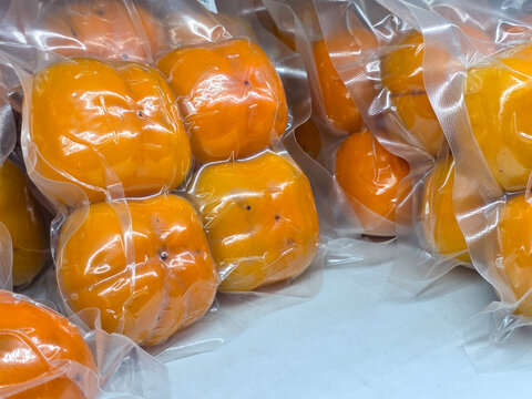 Vacuum packed persimmon fruit showing bright orange color, smooth skin, and fresh produce packaging, suitable for food storage, grocery retail, and healthy eating