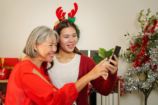 Asian mother and daughter pointing at smartphone screen during Christmas holiday at home