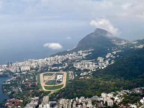 Aerial view of the Jockey Club Brasileiro racecourse surrounded by urban buildings and lush hills, with the Corcovado mountain in the background in Rio de Janeiro, Brazil.