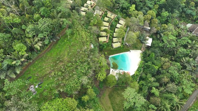 Aerial view of Glamping Menoreh featuring luxury tents nestled in lush tropical forest with a swimming pool in Kecamatan Samigaluh, Daerah Istimewa Yogya, Indonesia.