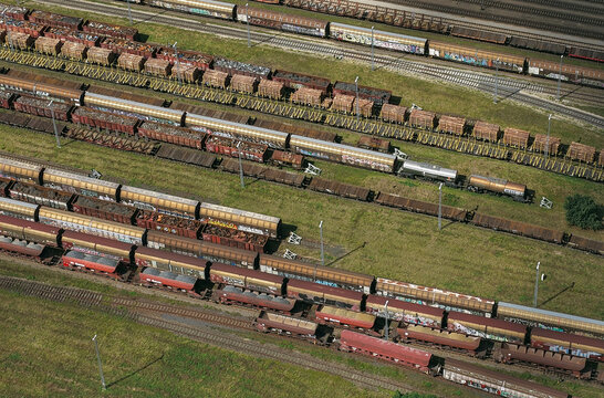 Aerial view of a large railway yard with multiple parallel tracks filled with freight trains, cargo cars, and graffiti in Saalfeld, Thuringia, Germany.