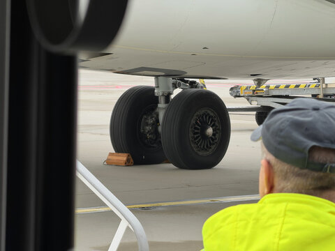 Commercial aircraft landing gear and large wheels on an airport apron during ground operations, with a ground service vehicle in the background.