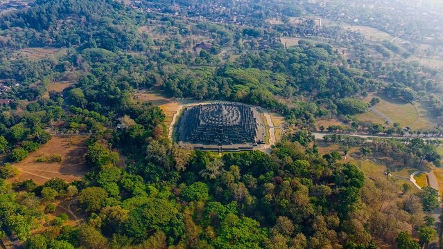 Aerial view of Borobudur Temple surrounded by lush green trees and tropical vegetation in Kecamatan Borobudur, Jawa Tengah, Indonesia.
