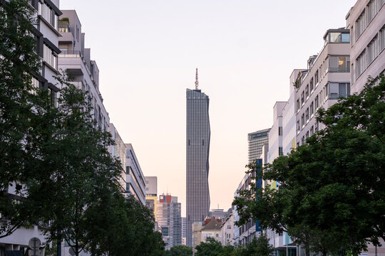 Street canyon frames a highrise tower between modern buildings and trees in Vienna, Austria, using architecture to create an urban perspective.