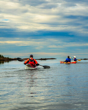 Vertical view of sea kayakers paddling toward distant islands under layered morning clouds, sky copy space above, Georgian Bay, Ontario