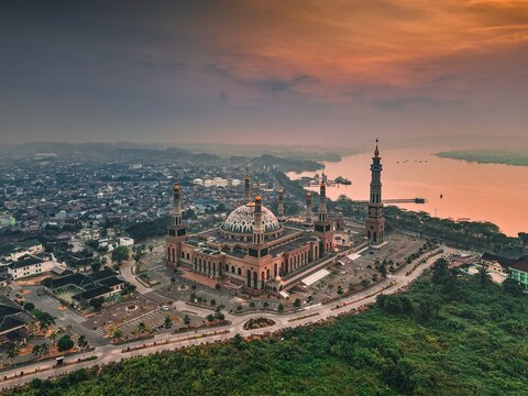 Aerial view of the Baitul Muttaqien Mosque at the East Kalimantan Islamic Center, featuring its grand dome and minarets near the river at sunset in Samarinda, East Kalimantan, Indonesia.