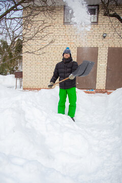 Man in winter jacket shoveling snow with shovel in front of brick house after heavy snowfall