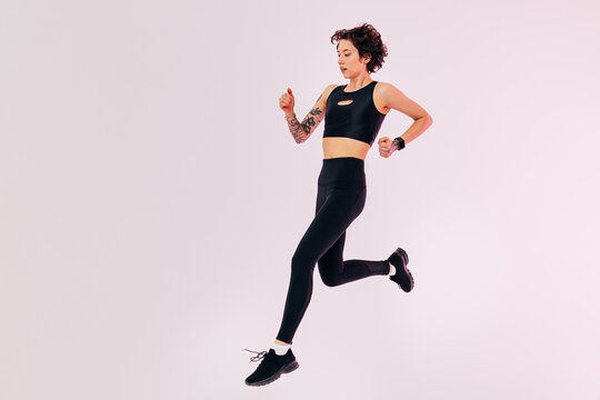 Full length of a young slim woman in black fitness wear jumping in a studio