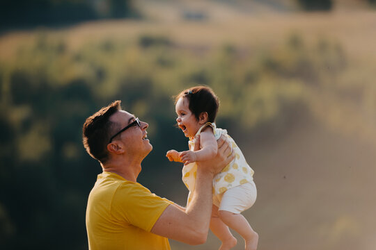 Father Lifting Laughing Baby Outdoors at Sunset &mdash; Playful Family Moment and Parental Joy