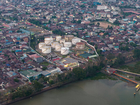 Aerial view of PT. Pertamina TBBM Samarinda fuel storage facility with white tanks near the river, surrounded by dense urban housing and rooftops in Samarinda, Kalimantan Timur, Indonesia.