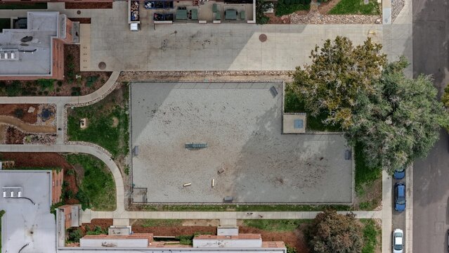 Aerial view of a fenced dog park in the Cherry Creek area with sandy ground, agility equipment, surrounding walkways, and mature trees in Denver, Colorado, United States.