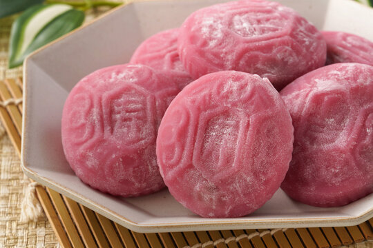 Traditional pink red turtle rice cake on woven grass mat background.