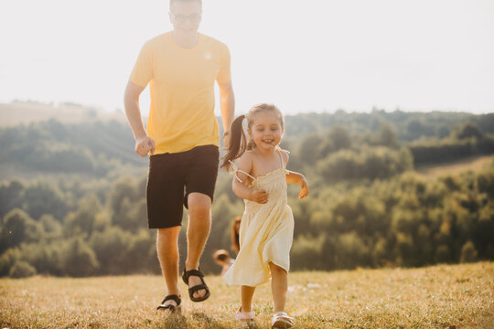 Father And Daughter Running Together In A Sunny Summer Meadow With Family Fun