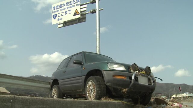 Wrecked Car Lies Under Warning Sign In Aftermath Of Tsunami In Japan