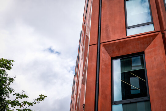 Modern Rust-Colored Building Facade with Tall Windows and Cloudy Sky