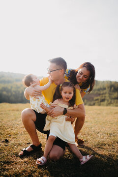 Happy Family Moment: Parents With Two Young Daughters Playing Outdoors in a Sunlit Meadow