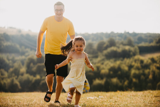 Father and Daughter Running Through a Sunlit Summer Meadow Together, Laughing and Playing Outdoors