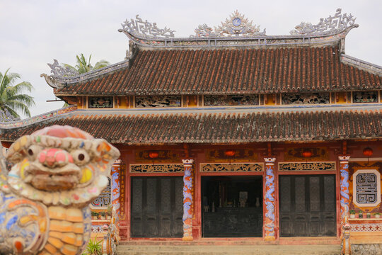 The main hall building of the historic Van Mieu Confucius Temple with a traditional ceramic stone lion statue in the blurred foreground in Hoi An, Vietnam.